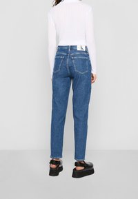 Modré džíny vysokého pasu se pravoúhlým střihem, které mají pět kapes a bílou značkovou visačku na pase.