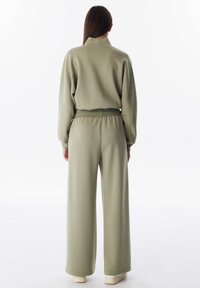 Olijfgroene sweatshirt met een relaxte pasvorm en wijde broek, gemaakt van zachte stof met een gladde textuur en geribbelde details bij de manchetten en tailleband.