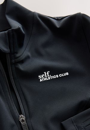 Črna športna jakna iz raztegljivega materiala. Ima visok ovratnik, zadrgo in bel logotip "self. ATHLETICS CLUB". Gladek tekstura.