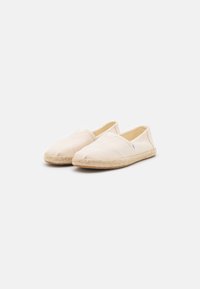 Beige espadrilles with a canvas upper and jute rope sole. Closed-toe design featuring subtle stitching and a slip-on style.