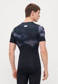 T-shirt de compression noire à manches courtes, avec une texture lisse et de subtils accents gris. Logo visible sur le haut du dos.
