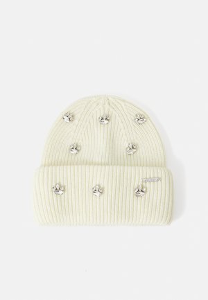 Berretto lavorato a maglia in bianco sporco con texture a costine, decorato con accenti di impronte di zampa in argento e un piccolo etichetta sul lato.