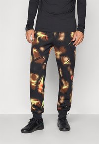 Black pants with a multicolored abstract pattern featuring orange, yellow, and brown splashes. Elastic waistband and cuffs.