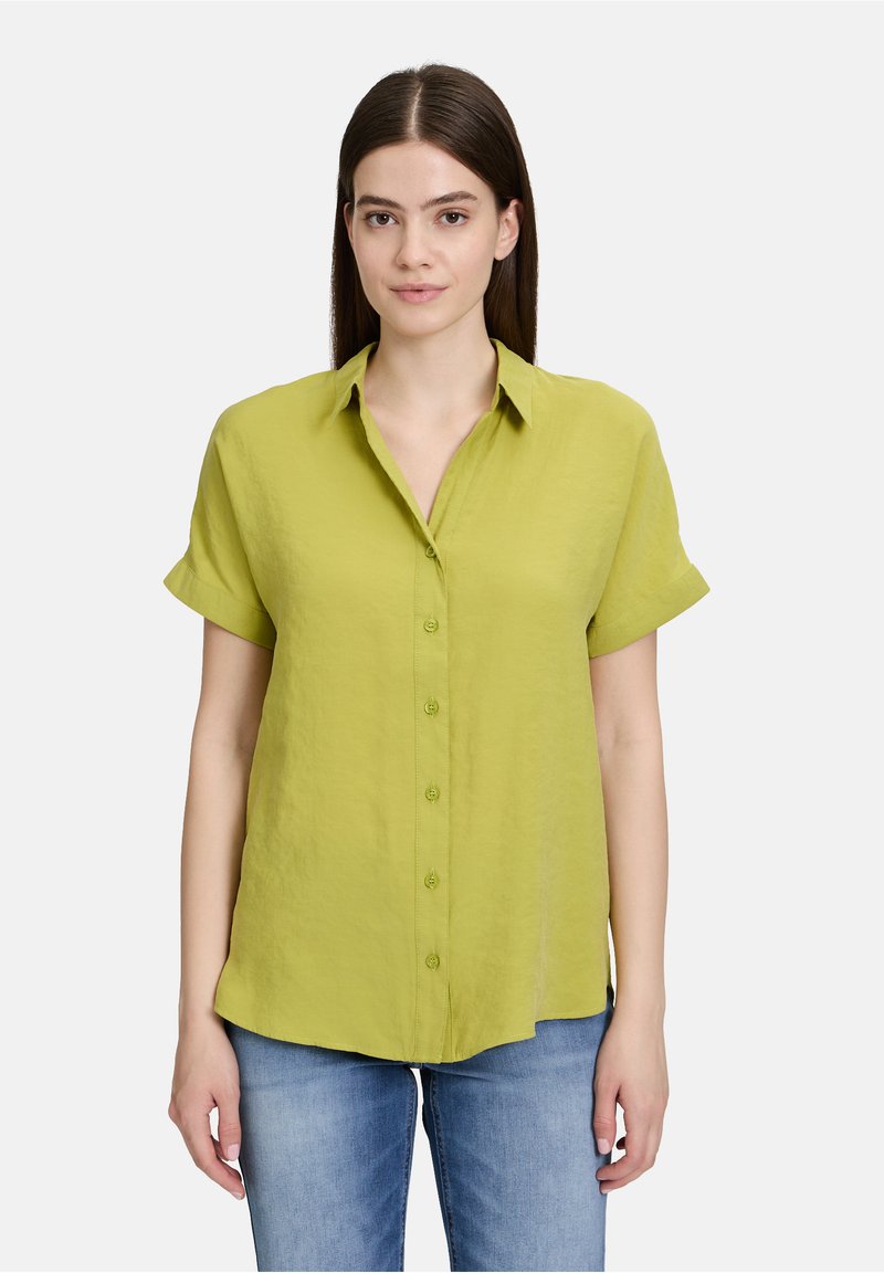 Korte mouwen, knoopshirt van fel limoen groen linnen. Bevat een kraag, opgerolde mouwen en een rechte zoom. Gemaakt met blauwe spijkerbroeken.