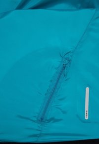 Gros plan d’un tissu bleu avec une fermeture éclair verticale et une petite étiquette rectangulaire avec des caractères japonais.