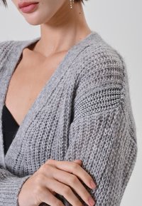 Cardigan grigio in maglia con scollo a V, lavorazione a trama e strisce argentate sulle maniche. Materiale morbido e leggero.