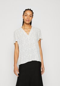 Blusa bianca a maniche corte con scollatura a V, caratterizzata da un motivo a pois neri. Tessuto morbido e leggero con una vestibilità ampia.