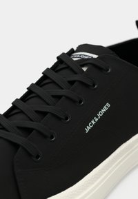 Schwarzer Low-Top Sneaker mit schwarzen Schnürsenkeln, weißer Sohle und "JACK & JONES"-Logo auf der Seite aufgedruckt.