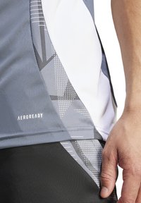 Maglietta sportiva grigia con un design geometrico testurizzato, pannelli in mesh bianco e una finitura in tessuto morbido. Logo "AEROREADY" visibile.