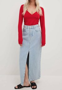 Rotes Langarmoberteil kombiniert mit einem hellblauen Jeans-Maxi-Rock mit einem Schlitz vorne. Schwarze flache Sandalen runden das Outfit ab.