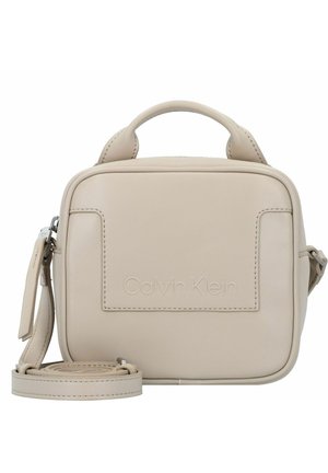 Malá béžová taška Calvin Klein přes tělo s horním uchem, přední kapsou a nastavitelným ramenním popruhem stočeným u základu.