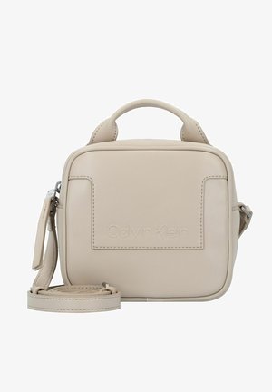 Petit sac bandoulière beige Calvin Klein avec poignée supérieure, poche avant et sangle d'épaule ajustable enroulée à la base.