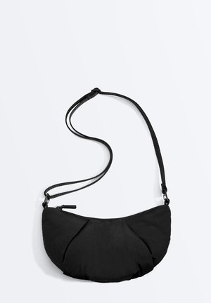 Kleine schwarze halbmondförmige Schultertasche mit verstellbarem Riemen und Reißverschluss, dargestellt auf einem einfarbigen hellen Hintergrund.