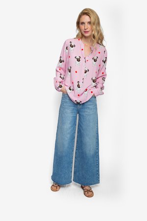 Roze overhemd met hondenprint en kleine rode accenten, gecombineerd met wijde blauwe spijkerbroeken en bruine sandalen met bandjes.