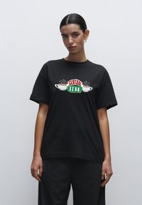 Černé bavlněné tričko s grafikou "CENTRAL PERK"; obsahuje bílé šálky kávy s párou. Uvolněný střih, krátké rukávy, kulatý výstřih.