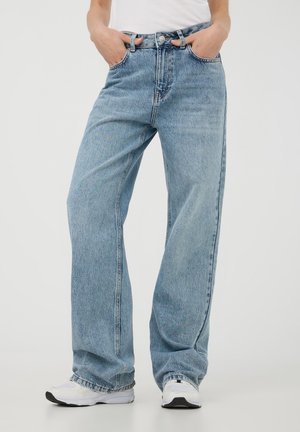 Jeans in denim azzurro chiaro a gamba larga con vita alta, cinque tasche e cuciture tono su tono. Indossati con un semplice top bianco e sneakers bianche.
