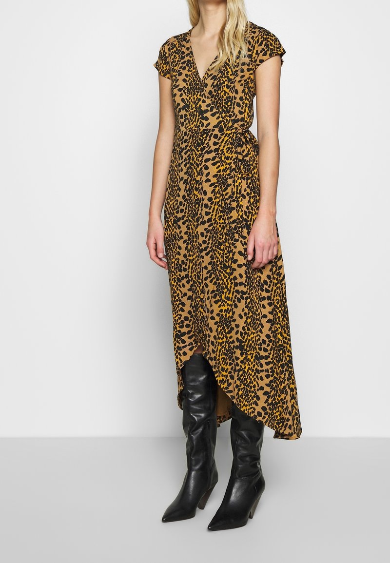 Femme portant une robe portefeuille à imprimé léopard marron et noir à manches courtes, associée à des bottes noires montantes à bout pointu.