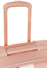 Maleta rodante con un exterior de melocotón mate, bandas de acento texturizadas, un mango retráctil y un compartimento con cremallera en la base.