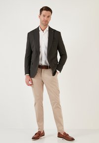 Blazer grigio scuro, camicia bianca, pantaloni beige, cintura marrone e mocassini marroni. Il blazer ha rever a punta e tasche laterali. Design pulito.
