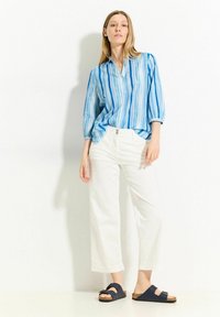 Camisa de botones a rayas azul y blanca, pantalones anchos blancos y sandalias navy de tipo slip-on con suela de corcho. Tejido suave, corte relajado.