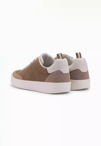 Bruna mockaskinnssneakers med vita läderdetaljer, platta snören och en strukturerad, ljus färgad sula. Baksidan har en ögla och subtil branding.