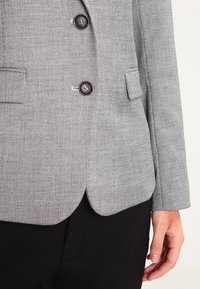 Gray houndstooth blazer with two black buttons, tailored fit, sharp lapels, and side pockets. Smooth texture with a classic pattern.