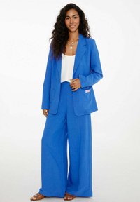 Modré sako a široké nohavice set, vyrobené z ľahkej tkaniny. Obsahuje predné vrecká a malú ružovú akcentovú etiketu. Hladká textúra.