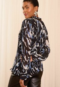 Zwarte en blauwe gebloemde blouse met een geplooide textuur, lange mouwen en manchetten, gecombineerd met hoge zwarte leren broek.
