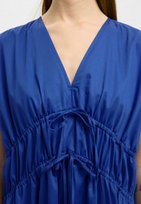Blaues Kleid aus glattem Stoff, mit V-Ausschnitt, geraffter Taille mit Bändern und schwingendem Rock für einen lässigen Sitz.