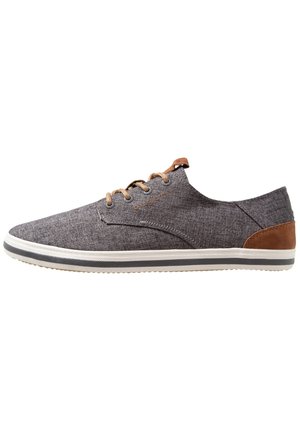 Szary, codzienny but sznurowany z tkaniny z beżowymi akcentami na pięcie i sznurowadłach, białą podeszwą z szarym paskiem oraz niskoprofilowym fasonem.