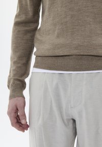 Suéter de punto beige con mangas largas, puños acanalados y dobladillo. Combinado con pantalones de corte relajado en gris claro, fabricados con un tejido suave.