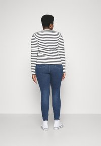 Pruhovaná košile s dlouhým rukávem v bílé a námořnické modři, spárovaná s modrými skinny džíny. Bílé tenisky s černými akcenty a volný střih.