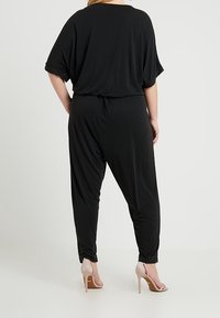 Czarny kombinezon o luźnym kroju, z krótkimi rękawami i talią z marszczeniem. Wykonany z miękkiej tkaniny, o gładkiej fakturze i szerokich nogawkach.