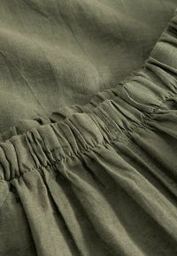 Εγγύς πλάνο υφάσματος ελιάς με συγκεντρωμένη ελαστική μέση που δείχνει υφή και λεπτομέρειες ραφής.