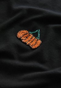 Tissu noir avec un design brodé de perles orange en forme de pile, rehaussé d'un contour de perles vertes.