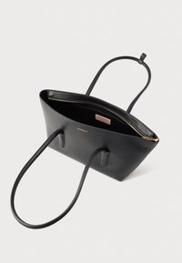 Borsa tote in pelle nera con manici lunghi, cerniera dorata e piccolo logo "COCCINELLE" dorato sulla parte anteriore.