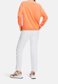 Pull en maille orange avec accents blancs, associé à un pantalon blanc et des baskets multicolores avec un design texturé et une semelle épaisse.