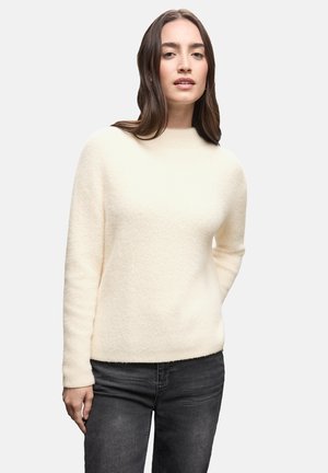 Jersey color crema con cuello alto, textura suave, mangas largas y un diseño sencillo, combinado con jeans oscuros.