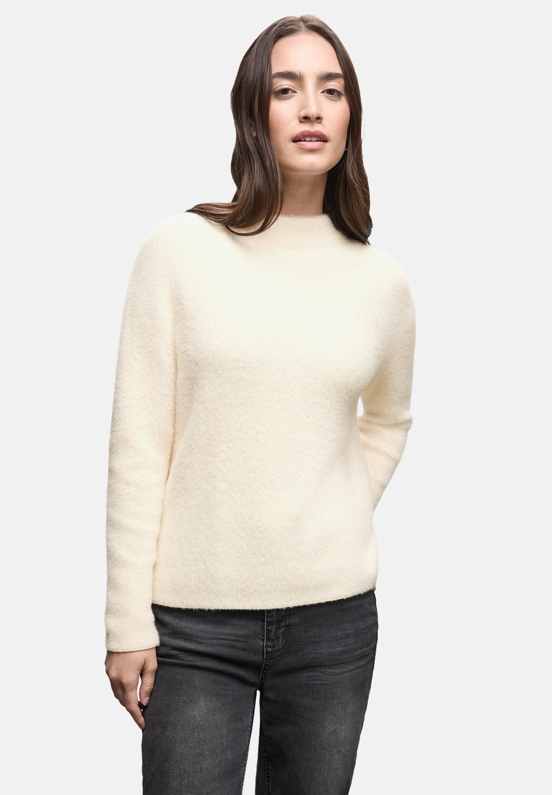 Cremfarbener Pullover mit hohem Kragen, weicher Textur, langen Ärmeln und einfachem Design, kombiniert mit dunklen Jeans.