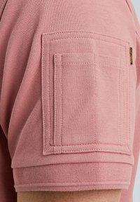 Pink short-sleeve shirt featuring a textured fabric, a patch pocket on the sleeve, and visible stitching details.