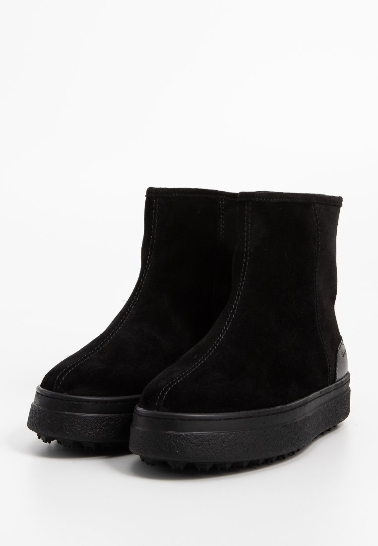 Schwarze Wildleder-Ankle Boots mit glatter Oberfläche, abgerundeter Zehenpartie und strukturierter schwarzer Gummisohle mit kleinen Traktionsnoppen.