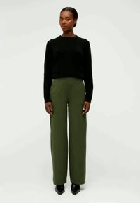 Black sweater, olive green wide-leg trousers, smooth fabric, minimal design, paired with black pointed-toe shoes, standing on a neutral background.