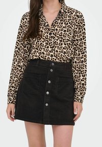 Lange mouwen blouse met luipaardprint, gecombineerd met een hoog opgesneden zwarte ribfluwelen rok met voorzakken en metalen knoopdetails.