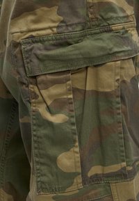 Gros plan de la poche à rabat avec des coutures détaillées d’un pantalon cargo camouflage vert et marron.
