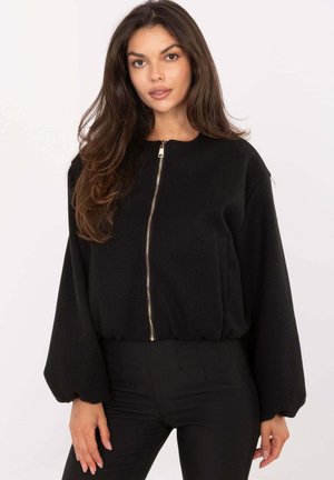 Black zipped jacket with a rounded neckline, balloon sleeves, elastic waistband, and side pockets, made from a soft fabric.