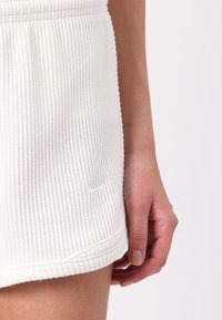 White ribbed shorts with a textured fabric, featuring a small embossed Nike logo on the hem and a fitted waistband.