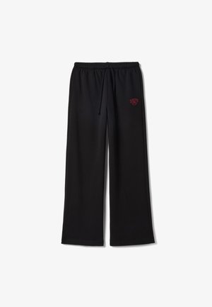 Pantalones de chándal negros con un ajuste holgado, cintura elástica, cordón ajustable y texto bordado en rojo en el lado izquierdo. Textura de tela suave.