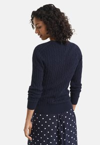 Maglione navy a maglia grossa con un motivo testurizzato, polsini e fondo a coste, abbinato a una gonna a pois, che mostra la vista dal retro.