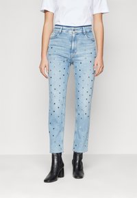 Ljusblå denimjeans med ankellängd, prydda med silverdetaljer och med en något fransig nederkant. Bärs med svarta ankle boots.