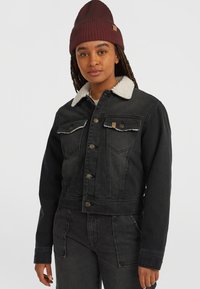 Sort denim cropped jakke med en shearling krave, frontknaplukning og to brystlommer. Båret med en mørk ribbet beanie.